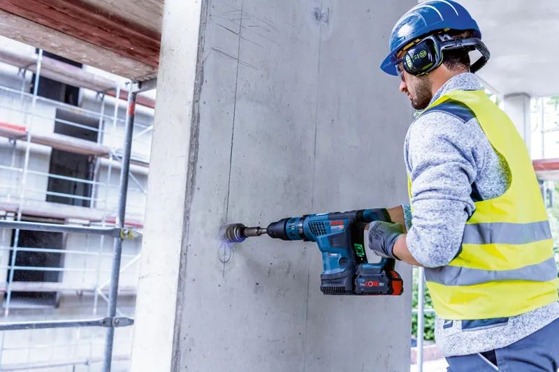 Une personne portant un équipement de sécurité utilise un marteau perforateur sans fil pour percer du béton.