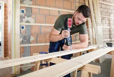Une personne portant un équipement de sécurité utilise un outil électrique pour couper une planche de bois sur un établi.