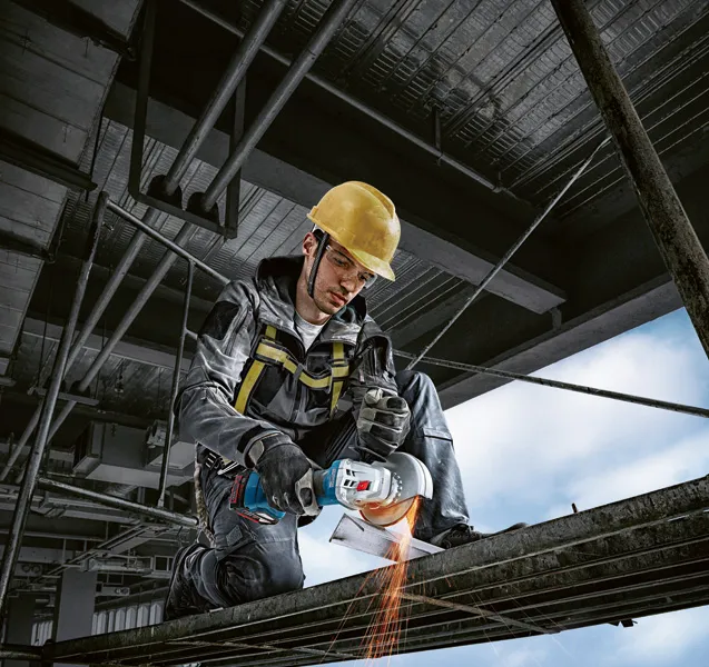 Une personne portant un équipement de sécurité broie du métal, créant des étincelles sur un chantier de construction.
