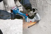 Une personne portant un équipement de sécurité utilise une meuleuse d’angle pour couper une barre d’armature dans le béton.