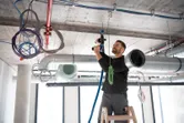 Une personne portant un équipement de sécurité utilise une perceuse avec adaptateur FlexiClick au-dessus d'une échelle.