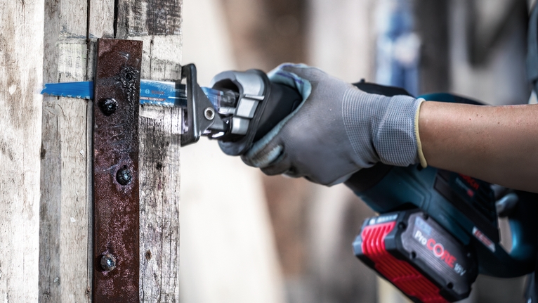 Une personne portant un équipement de sécurité utilise une scie alternative pour couper du métal sur du bois.