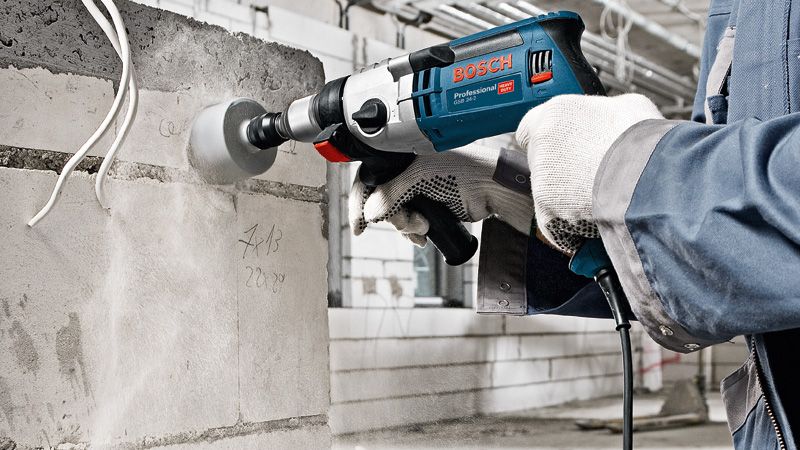Une personne portant un équipement de sécurité perce un trou dans un mur en béton avec un outil électrique.