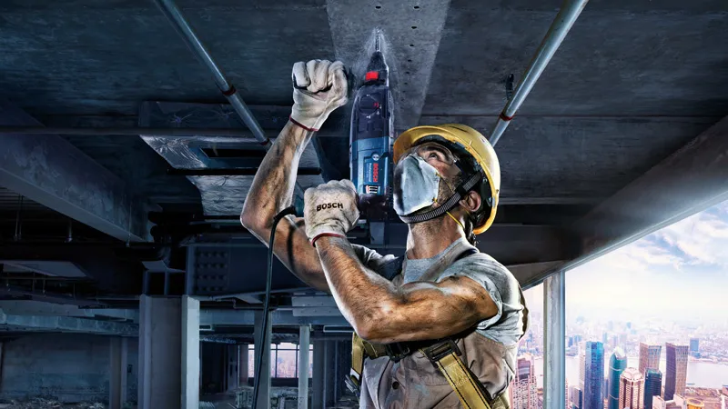 Une personne portant un équipement de sécurité perce un plafond en béton sur un chantier de construction.