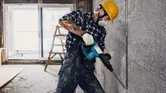Une personne portant un équipement de sécurité utilise un marteau de démolition pour briser un mur en béton.