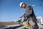 Une personne portant un équipement de sécurité coupe du bois avec une scie circulaire sur un chantier de construction.
