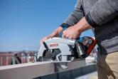 Une personne utilise une scie circulaire pour couper une planche de bois à l'extérieur.