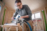 Une personne portant un équipement de sécurité utilise une scie circulaire pour couper du bois dans un atelier.