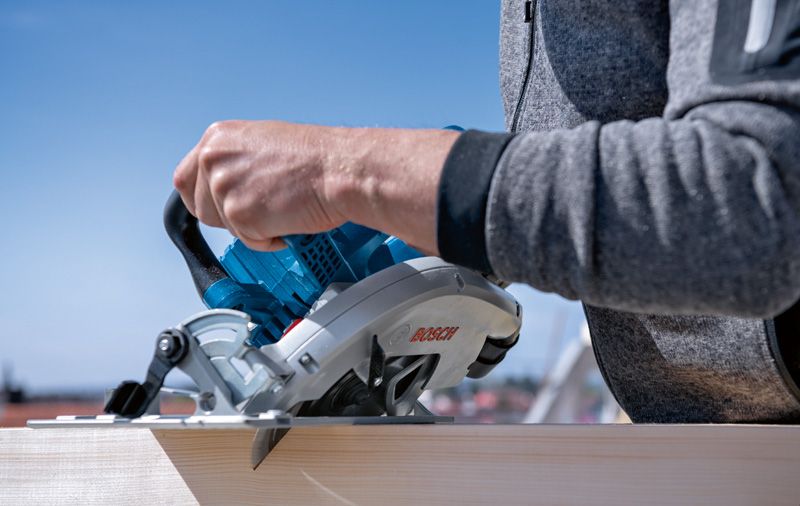 Une personne utilise une scie circulaire pour couper du bois à l'extérieur.
