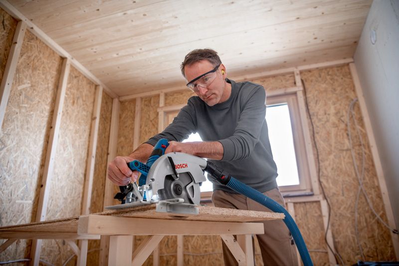 Une personne portant un équipement de sécurité utilise une scie circulaire pour couper du bois dans un atelier.