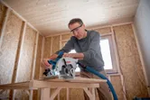 Une personne portant un équipement de sécurité utilise une scie circulaire pour couper du bois dans un atelier.