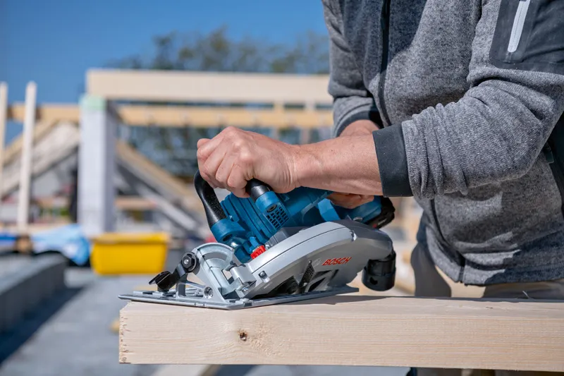 Une personne utilise une scie circulaire pour couper une poutre en bois sur un chantier de construction.