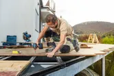 Une personne portant un équipement de sécurité perce des planches de terrasse sur un cadre de patio extérieur.
