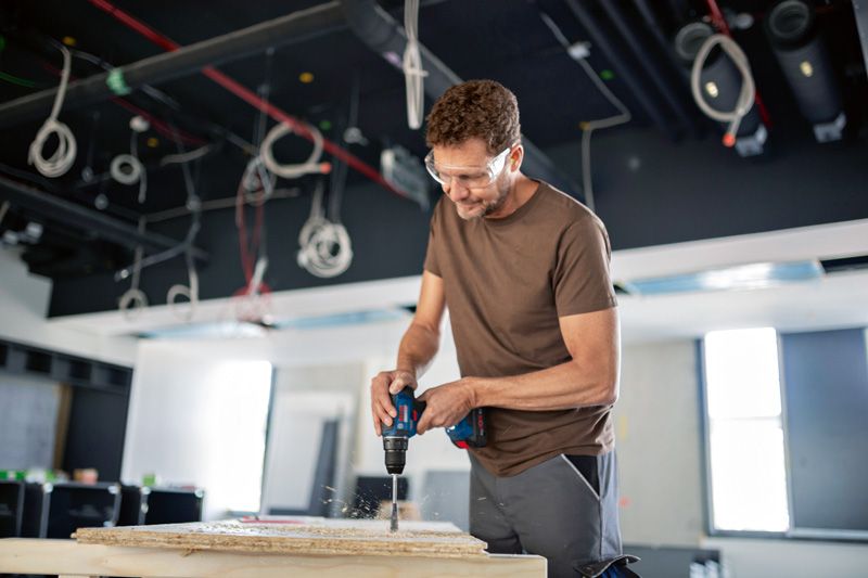Une personne portant un équipement de sécurité perce du bois sur un chantier de construction.