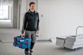 Personne portant un système de mallette de transport empilable bleu avec loquet dans une zone de construction.