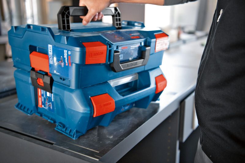 Personne soulevant un système de mallette de transport bleue empilée avec des loquets orange sur une table.