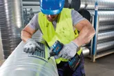 Une personne portant un équipement de sécurité fixe un couvercle d’aération sur un grand conduit métallique.