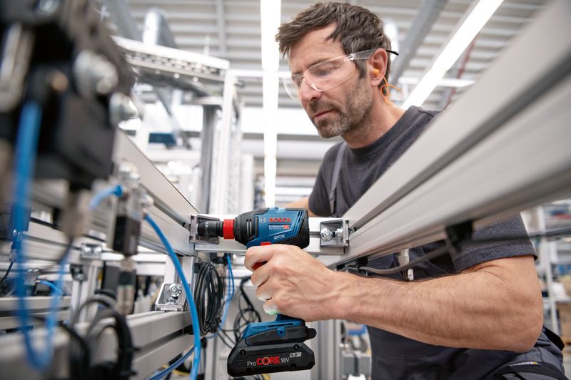 Une personne portant un équipement de sécurité utilise une perceuse sans fil pour fixer une structure métallique.