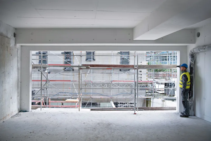 Une personne portant un équipement de sécurité utilise un télémètre laser sur un bâtiment en construction.