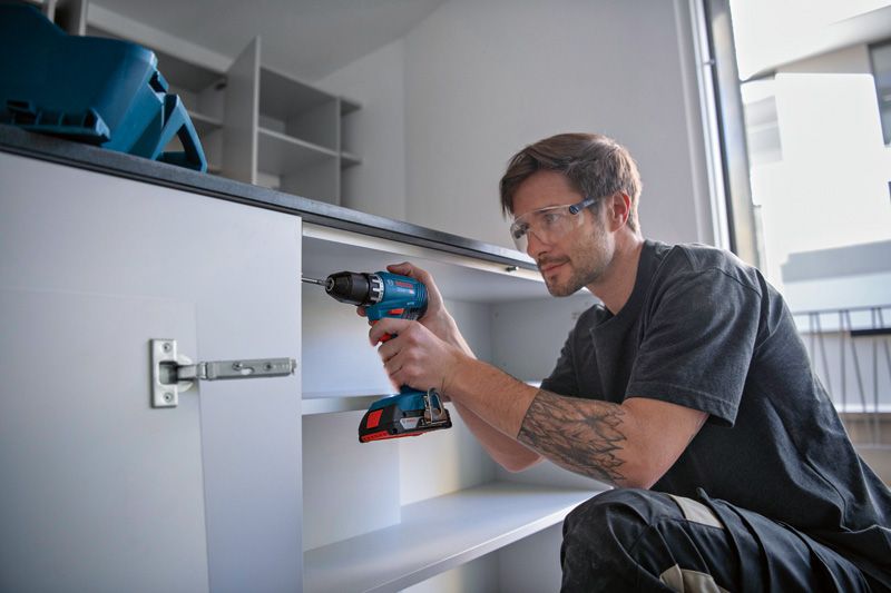 Une personne portant un équipement de sécurité perce le cadre d'une armoire.