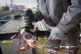 Une personne portant un équipement de sécurité meule une barre métallique avec une meuleuse d'angle portative.