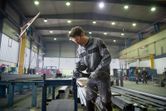 Une personne portant un équipement de sécurité broie du métal, des étincelles jaillissent dans un grand atelier industriel.