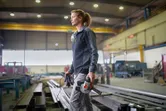 Une personne portant un équipement de sécurité porte une meuleuse d'angle dans un grand atelier industriel.