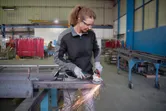 Une personne portant un équipement de sécurité utilise une meuleuse d’angle pour couper du métal, créant ainsi des étincelles.