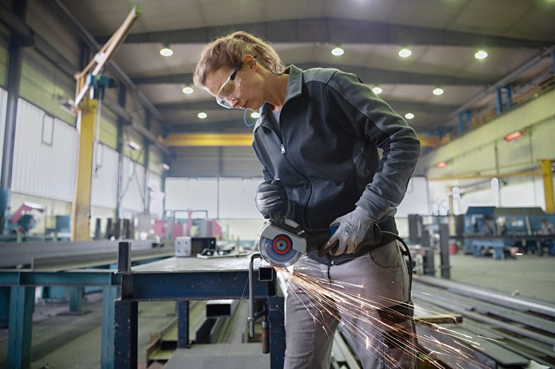 Une personne portant un équipement de sécurité meule du métal sur un établi, produisant des étincelles.