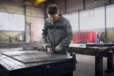 Une personne portant un équipement de sécurité utilise une meuleuse d’angle sur une table de travail en métal.