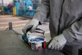 Une personne portant un équipement de sécurité fixe un disque à une meuleuse d'angle sur un établi.