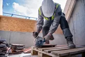 Une personne portant un équipement de sécurité découpe des tuiles de toit à l'aide d'une meuleuse d'angle sans fil.