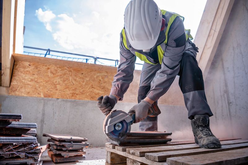 Un ouvrier portant un équipement de sécurité utilise une meuleuse d'angle sans fil pour couper des carreaux.