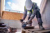 Un ouvrier portant un équipement de sécurité utilise une meuleuse d'angle sans fil pour couper des carreaux.