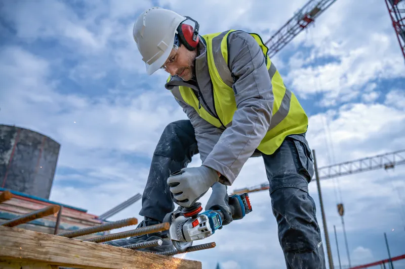 Une personne portant un équipement de sécurité broie des barres d'armature avec un outil électrique sur un chantier de construction.