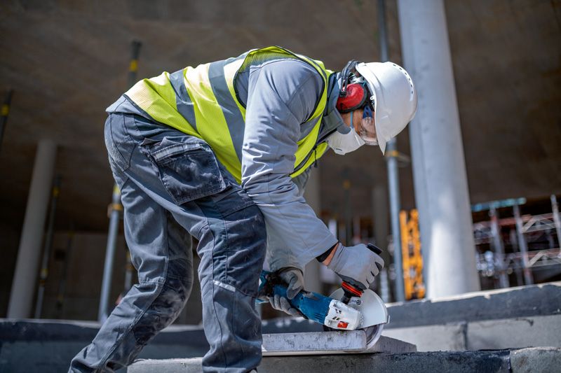 Une personne portant un équipement de sécurité utilise une meuleuse d'angle sans fil pour découper une dalle de béton.