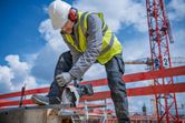 Une personne portant un équipement de sécurité coupe une poutre métallique sur un chantier de construction.