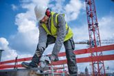 Une personne portant un équipement de sécurité découpe du métal sur un chantier de construction à l'aide d'une meuleuse d'angle sans fil.