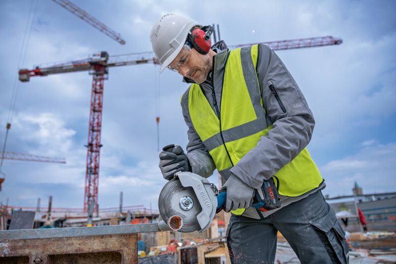 Une personne portant un équipement de sécurité utilise une meuleuse d'angle sans fil pour couper du métal sur un chantier de construction.