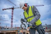 Une personne portant un équipement de sécurité utilise une meuleuse d'angle sans fil pour couper du métal sur un chantier de construction.
