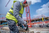 Une personne portant un équipement de sécurité utilise une meuleuse d'angle sans fil pour couper des barres d'armature sur un chantier de construction.