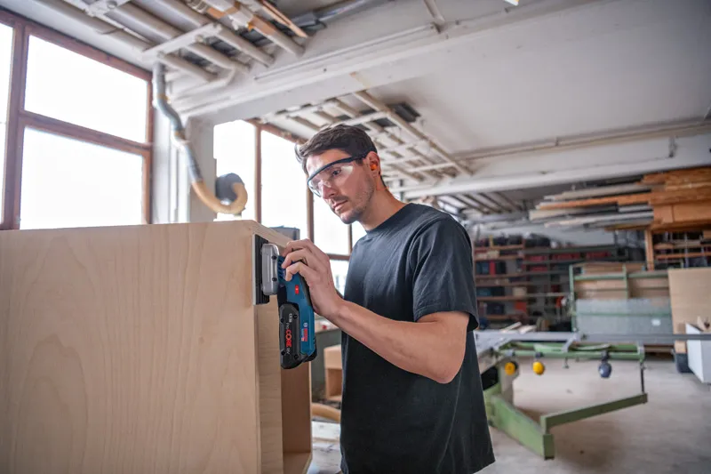 Dans un atelier, une personne portant un équipement de sécurité ponce le bord d'une armoire en bois.