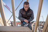 Une personne portant un équipement de sécurité utilise une scie électrique pour couper du bois sur un chantier de construction.
