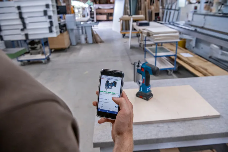 Une personne utilise un smartphone pour référencer une perceuse sans fil dans un atelier de menuiserie.