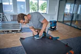 Une personne portant un équipement de sécurité utilise une scie sauteuse pour couper une feuille sur un établi.