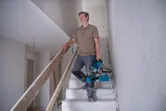 Une personne porte une scie à onglet dans un escalier à l'intérieur d'un bâtiment inachevé.