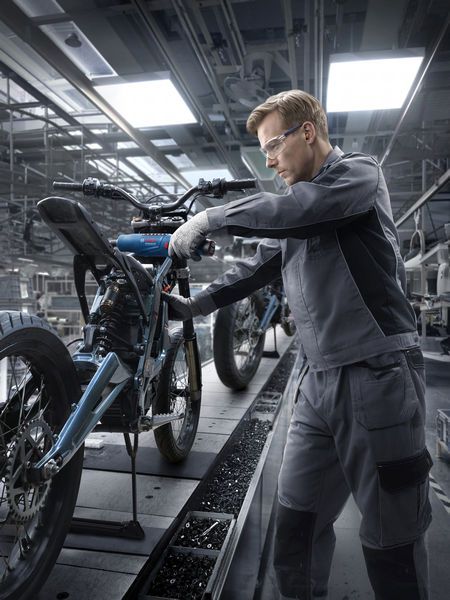 Une personne portant un équipement de sécurité assemble un cadre de moto dans une usine.