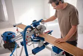 Une personne portant un équipement de sécurité coupe une planche de bois avec une scie à onglet.