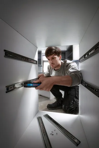 Une personne utilise un tournevis sans fil pour installer des glissières de tiroir à l’intérieur d’une armoire.