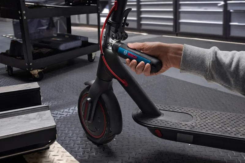 Une personne utilise un tournevis sans fil pour régler le guidon d’un scooter électrique.